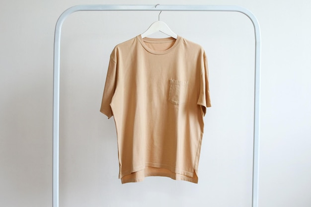 Maqueta de camiseta de algodón beige sencilla colgada en un colgante blanco en el estante vista delantera