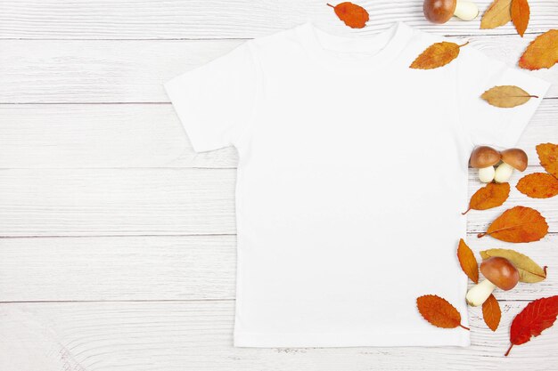 Maqueta de camiseta de algodón blanco para mujer con champiñones y hojas caídas sobre fondo de madera blanca Plantilla de camiseta de diseño maqueta de presentación de impresión Vista superior plana