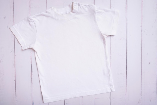 Maqueta de camiseta blanca para niños para texto o diseño de logotipo en la vista superior de fondo de madera