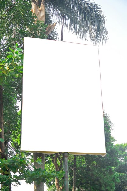 Maqueta de cartelera vertical en blanco o calle de la bandera colgada en el poste de hormigón cerca del árbol