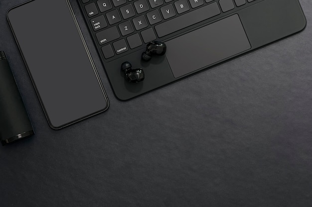 Maqueta de color negro de teléfono inteligente, teclado de computadora y auriculares en la mesa superior de cuero negro.