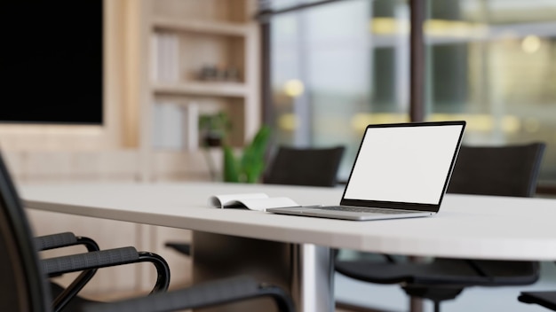 Una maqueta de computadora portátil de pantalla blanca en una mesa de reuniones blanca en una sala de reuniones minimalista moderna