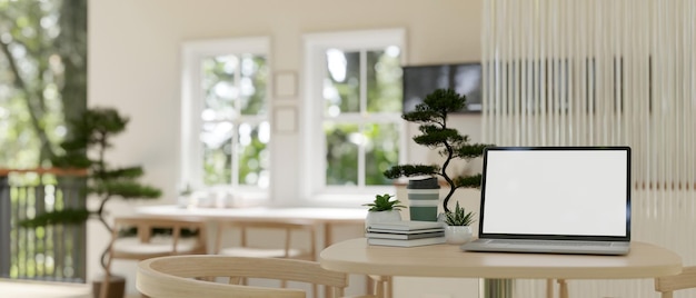 Una maqueta de una computadora portátil con pantalla blanca sobre una mesa de madera en una sala de estar minimalista y luminosa