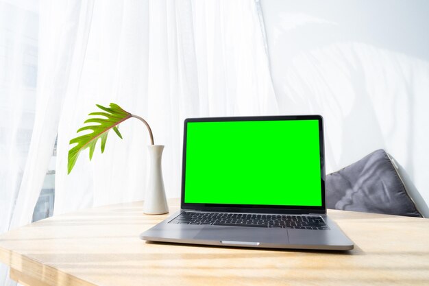 Maqueta de computadora portátil con pantalla vacía con taza de café y teléfono inteligente en la mesa de la cafetería al aire libre fondo Pantalla verde