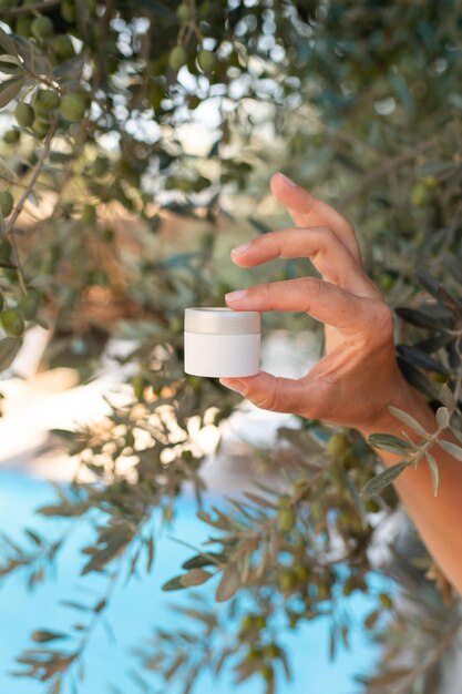 Maqueta de crema de piel, tubo blanco en manos femeninas sobre fondo de olivo, seguridad de la piel