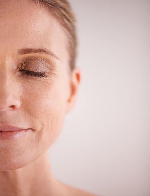 Maqueta de cuidado de la piel y mitad con una cara de mujer en estudio sobre un fondo gris para publicidad de belleza cosmética Bienestar facial y ojos cerrados con una modelo femenina senior posando para el cuidado natural de la piel