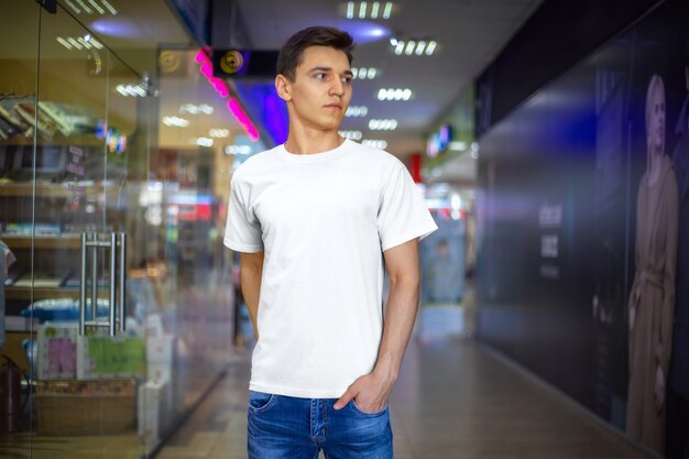 Maqueta de diseño de camiseta blanca y lugar para su patrón. Plantilla de ropa en un chico joven y en el fondo de la tienda. Vista frontal.