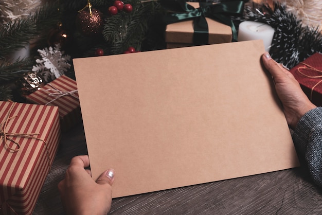 Maqueta de diseño de papel de saludo de vacaciones de Navidad con decoración en mesa de madera.