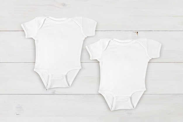 Maqueta de dos onesies de bebé blanco sobre fondo de madera blanca contemporánea