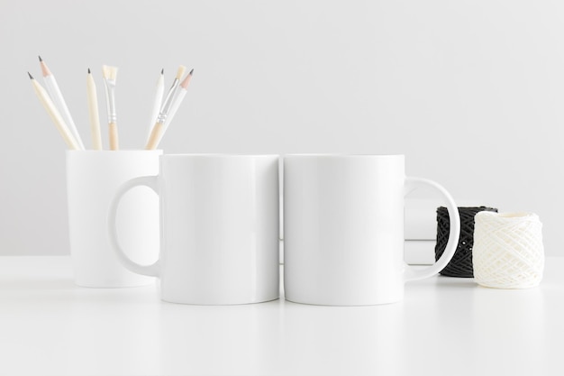 Foto maqueta de dos tazas con accesorios de espacio de trabajo en una mesa blanca