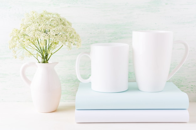 Maqueta de dos tazas blancas con libros y flores blancas en la jarra