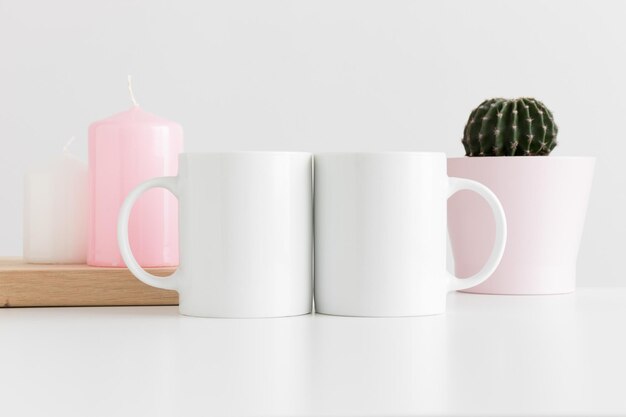 Maqueta de dos tazas con velas y un cactus en una olla sobre mesa blanca