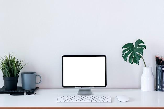 Maqueta de espacio de trabajo creativo con tableta de pantalla en blanco en el soporte y teclado en la mesa superior blanca.