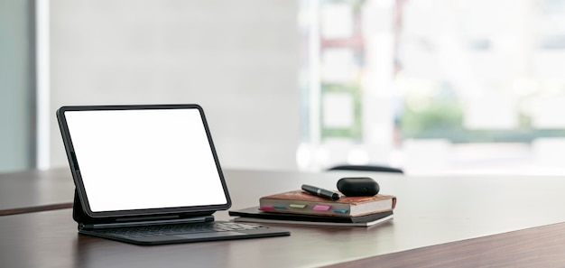 Maqueta de espacio de trabajo tableta digital de pantalla en blanco abierta con teclado mágico en escritorio de madera en banner de sala de oficina