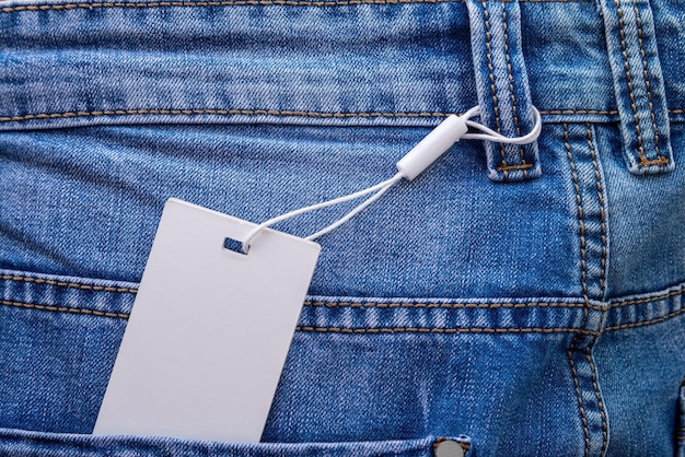 Maqueta de una etiqueta de papel en blanco con cordón blanco colocado en blue jeans.