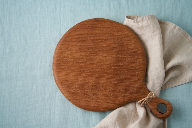 Maqueta de fondo de alimentos con tabla de cortar de madera redonda sobre fondo de mantel textil de lino azul