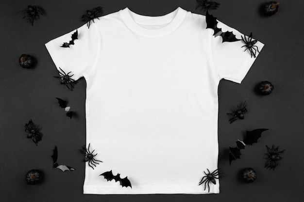 Maqueta de halloween de camiseta blanca de algodón para mujer con calabazas, arañas y murciélagos sobre fondo negro Plantilla de camiseta de diseño maqueta de presentación de impresión Vista superior plana