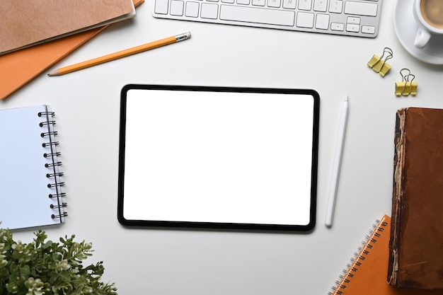 Maqueta horizontal de tableta digital con pantalla en blanco rodeada de suministros de oficina en el escritorio de oficina blanco.