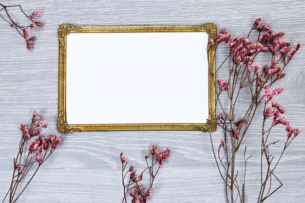 Maqueta de imagen dorada o marco de fotos con gypsophila de aliento de bebé rosa sobre una mesa de madera gris