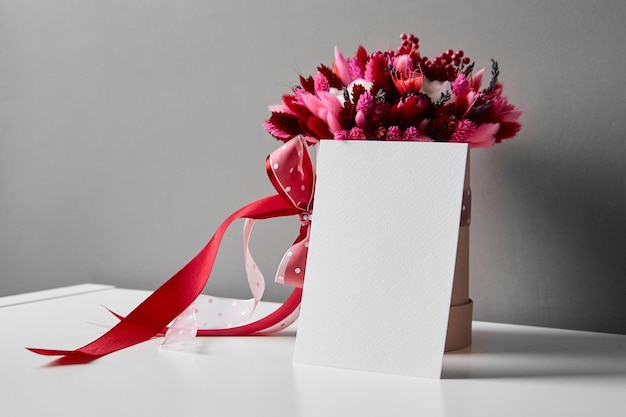 Maqueta de invitación o tarjeta de felicitación y ramo de flores secas en mesa blanca