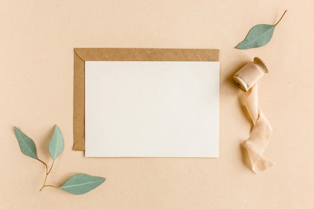 Maqueta invitación tarjeta de felicitación en blanco y sobre artesanal hojas verdes eucalipto vista plana endecha superior