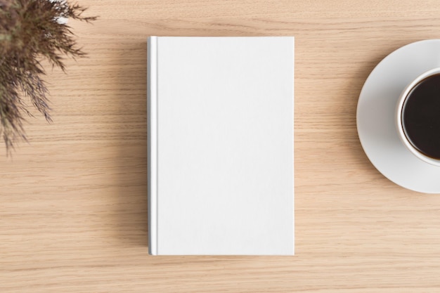 Maqueta de libro blanco con una flor seca y una taza de café en la mesa de madera