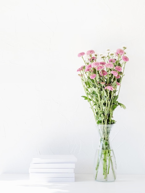 Maqueta de libro blanco con flores de crisantemo en un jarrón sobre una mesa blanca