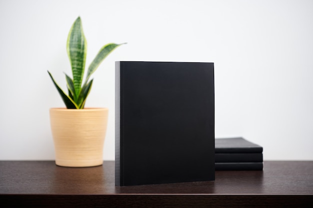 Foto maqueta de libro negro con cactus en una maceta en la mesa de espacio de trabajo oscuro y fondo de pared blanca