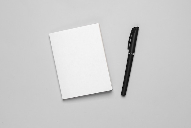 Maqueta de libro o bloc de notas con pluma de cubierta blanca sobre fondo gris plantilla para el diseño