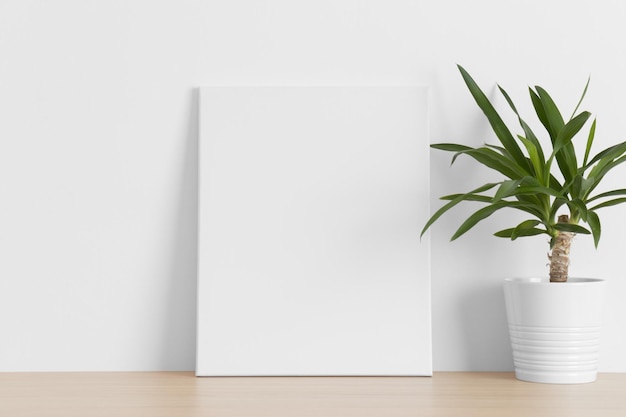 Maqueta de lienzo blanco con una planta de yuca en la mesa de madera