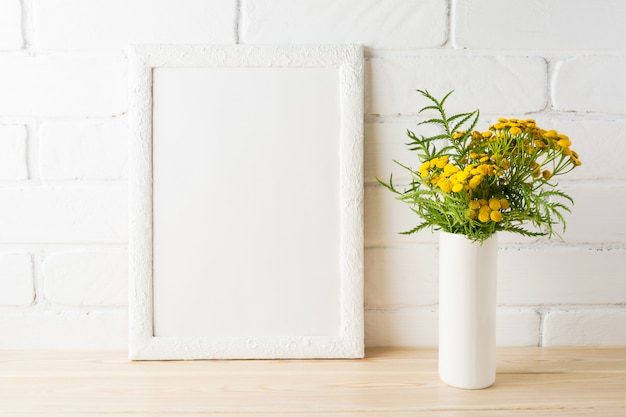 Maqueta de marco blanco con flores amarillas cerca de paredes de ladrillo pintadas