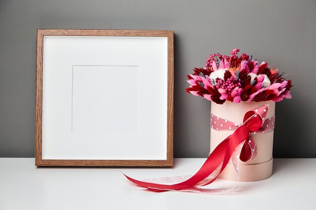 Maqueta de marco de foto o obra de arte y flores secas sobre fondo de pared gris