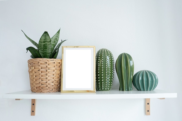 Maqueta de marco de fotos dorado en un estante con flores de interior y figuras de cactus.