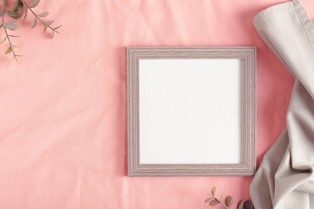 Maqueta de marco de fotos vacío y ramas en la vista superior de tela de algodón rosa