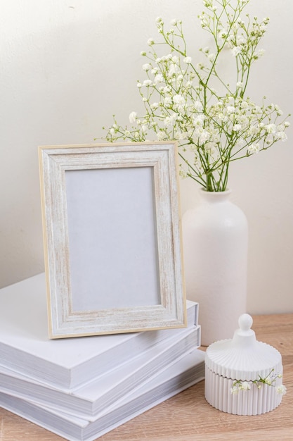 Maqueta de marco de imagen blanca de retrato en mesa de madera jarrón de cerámica moderno con gypsophilascandinavian