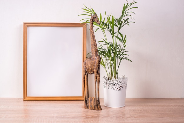 Maqueta de marco de imagen broun retrato en mesa de madera. Decoración de madera con figura de jirafa y palmera. Fondo de pared blanca. Interior escandinavo.