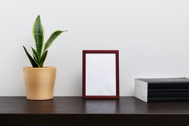 Maqueta de marco de madera marrón en orientación vertical con un cactus en una maceta y un libro sobre la mesa del espacio de trabajo oscuro y fondo blanco