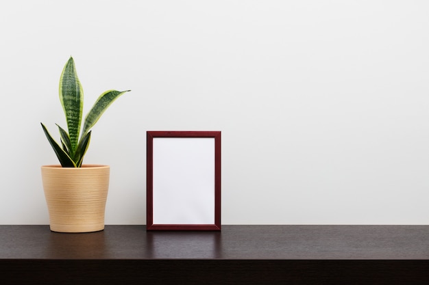 Maqueta de marco de madera marrón en orientación vertical con un cactus en una maceta en la mesa del espacio de trabajo oscuro y fondo blanco