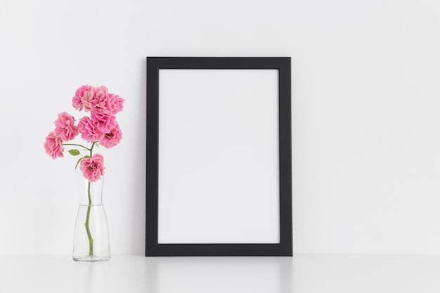 Maqueta de marco negro con rosas rosadas en un jarrón de vidrio sobre una mesa blancaOrientación vertical