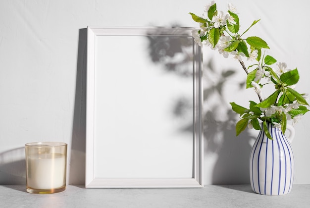 Maqueta de marco vacío con flores de árbol en florero y vela perfumada