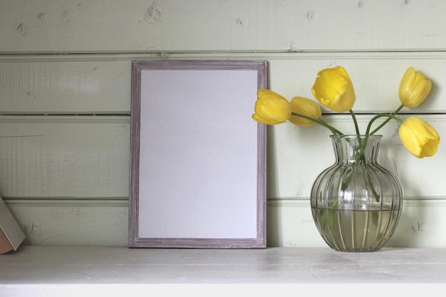 Una maqueta de un marco vacío y un ramo de tulipanes amarillos en la mesa Copiar espacio