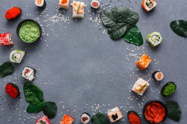 Maqueta para el menú del restaurante japonés, rollos de sushi y plato de gunkan. Marco redondo de hojas verdes, jengibre, soja sobre fondo gris rústico y arroz. Vista superior, espacio de copia