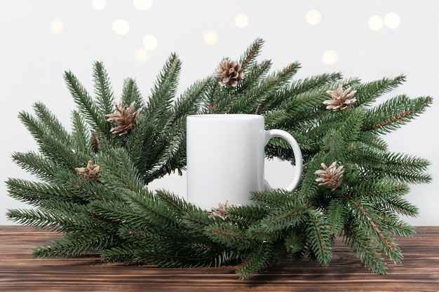 Maqueta de Navidad una taza de té vacía blanca sobre una mesa de madera marrón y ramas de una corona de árbol de Navidad. Plantilla de taza para su diseño, logotipo con espacio de copia. Año nuevo