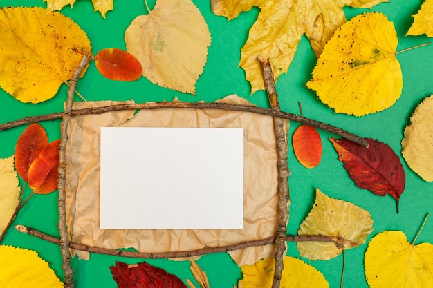 Foto maqueta de otoño con hojas amarillas y rojas. conos de abeto y una hoja blanca de papel para la inscripción.