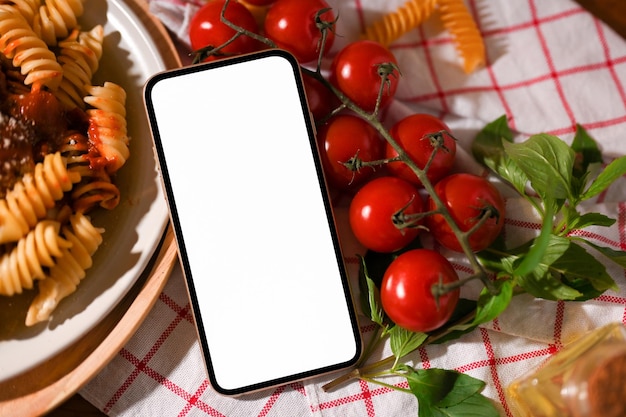 La maqueta de la pantalla blanca del teléfono inteligente está en una mesa de comedor con un plato de pasta