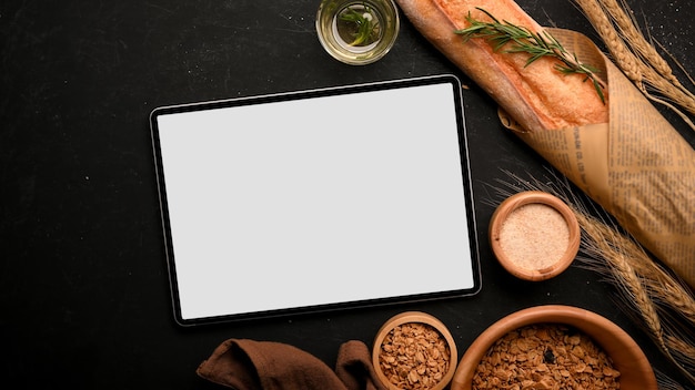 Maqueta de pantalla en blanco de la computadora del panel táctil de la tableta con pan francés o baguette sobre fondo negro