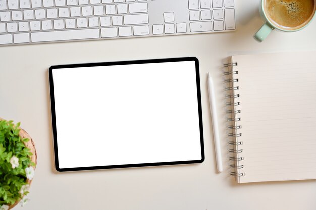 Maqueta de pantalla de tableta digital en blanco con bloc de notas en blanco, teclado de lápiz óptico en la mesa de trabajo blanca