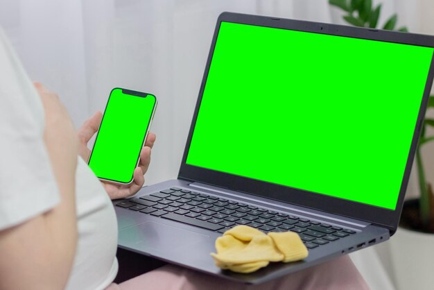 Maqueta de pantalla verde de teléfono y computadora portátil Mujer embarazada mirando la computadora portátil y el teléfono con clave de croma