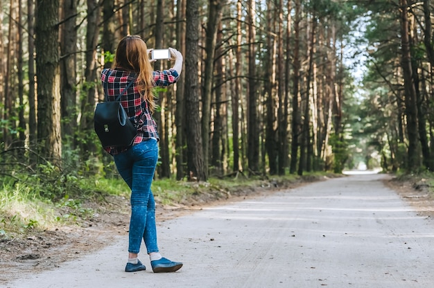 Maqueta de smartphone en las manos Chicas en el bosque, sobre un fondo de árboles. Concepto sobre el tema de la recreación al aire libre de viajes.