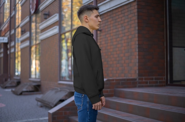 Maqueta de una sudadera con capucha negra en un chico joven en jeans, vista lateral. Plantilla de ropa casual para presentación de diseño y patrón. Campana vacía con mangas para publicidad en la tienda online